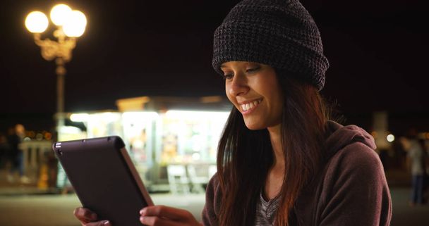 Millennial valkoihoinen tyttö käyttää tabletti tietokone kaupungin kadulla yöllä
 - Valokuva, kuva