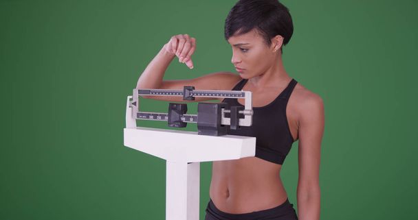 gesunde junge schwarze Frau, die auf einer Waage steht, um sich auf einem grünen Bildschirm zu wiegen - Foto, Bild