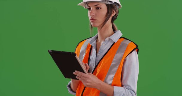 Mujer en chaleco naranja con dispositivo de tableta y hardhat trabajando en pantalla verde
 - Foto, imagen