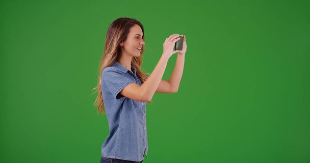 Atractiva hembra blanca tomando fotos con la cámara del teléfono en la pantalla verde
 - Foto, Imagen