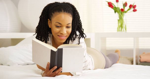 Young black woman reading on bed - Foto, imagen