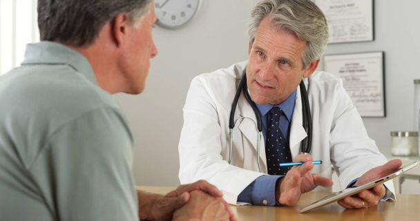 Médico senior hablando con paciente y tableta en el consultorio
 - Foto, imagen