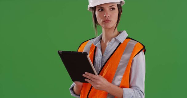 Női építőmunkás narancssárga mellény és a védősisak használata pad, a zöld képernyő - Fotó, kép