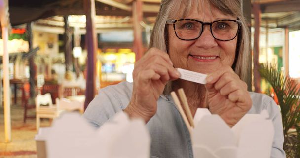 Portret van gelukkig senior vrouw lezen van fortuin na het eten van Chinees eten buiten - Foto, afbeelding