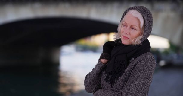Ανώτερων γυναίκα σε πουλόβερ και κασκόλ Κοιτάζοντας πέρα από τον ποταμό Σηκουάνα στο Παρίσι διακοπές - Φωτογραφία, εικόνα