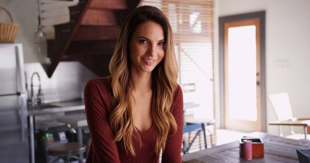 Attractive female millennial sitting inside kitchen smiling at camera - Photo, Image