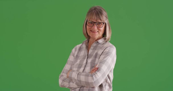 Happy senior woman smiling with arms crossed standing on green screen - Photo, Image