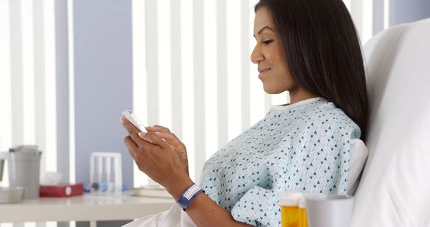 病院のベッドでスマート フォンを使用しての黒人女性 - 写真・画像
