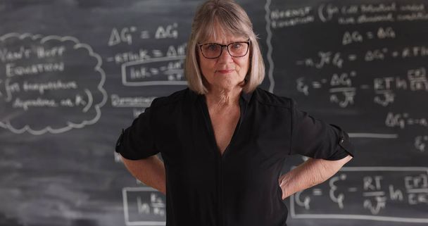 Old senior woman teacher with serious attitude posing in front of chalkboard - Photo, Image