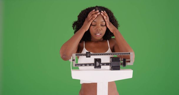 Молодая черная женщина, взвешивающая себя, разочарована ростом веса на зеленом экране
 - Фото, изображение