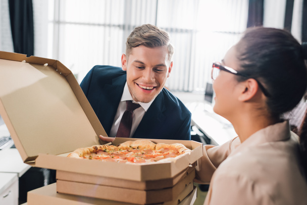 jeune femme d'affaires tenant des boîtes à pizza et homme d'affaires souriant regardant la pizza savoureuse
 - Photo, image