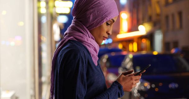 Jonge moslimvrouw op stedelijke straat bij nacht texting - Foto, afbeelding