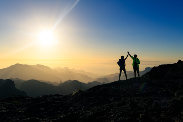 Pár turistů slaví úspěch v sunset mountains, dosáhnout rukama nahoru natažené. Mladý muž a žena při pohledu na krásné inspirativní na šířku, Kanárské ostrovy Gran Canaria. - Fotografie, Obrázek