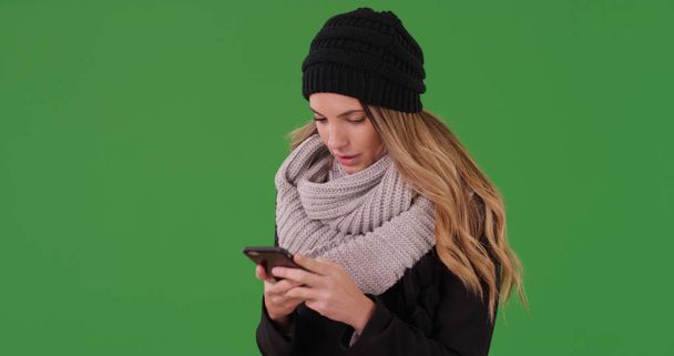 Millennial woman in winter clothes texting on smartphone on green screen - Photo, Image