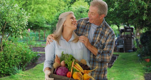 Happy aged white gardener couple stand proudly with produce from private garden - Photo, Image