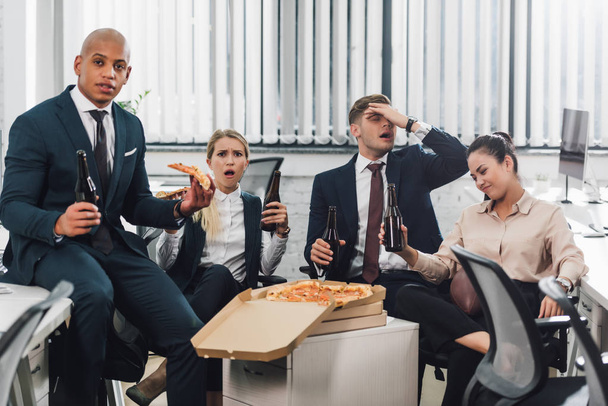 эмоциональные молодые бизнесмены пьют пиво и едят пиццу в офисе
  - Фото, изображение