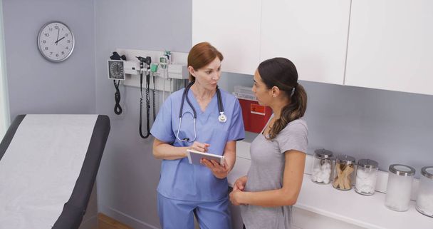 Attractive female hispanic patient looking at tablet device with nurse - Foto, Imagen