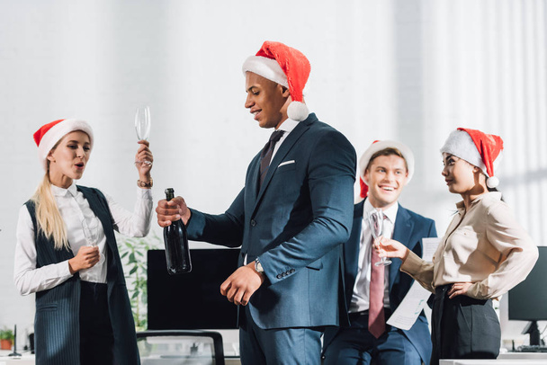 事務所でクリスマスを祝っているサンタ帽子で幸せな若い混血同僚     - 写真・画像