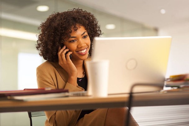 Millennial  businesswoman using laptop computer while talking on phone. - Φωτογραφία, εικόνα