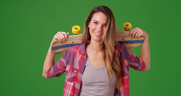 Porträt eines lächelnden Millennial-Mädchens, das mit Skateboard auf grünem Bildschirm posiert - Foto, Bild