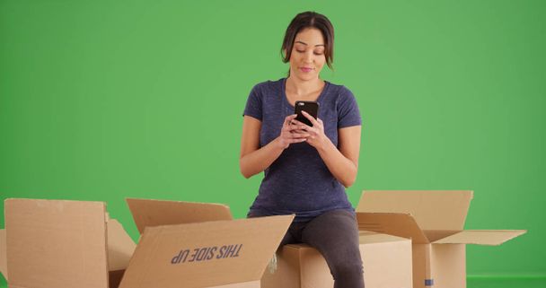 Frau macht Pause beim Auspacken von Kisten mit Handy auf grünem Bildschirm - Foto, Bild