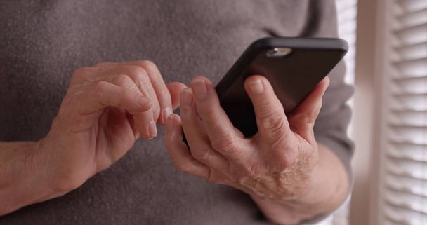 国内設定のウィンドウが携帯電話に古い女性の手のテキスト メッセージがタイトなショットします。 - 写真・画像