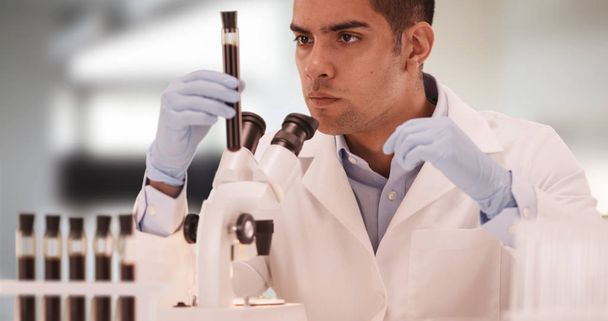Millennial Hispanic medical scientist in laboratory looking through microscope - Photo, Image
