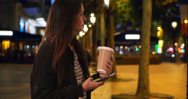 Hipster girl on the Champs-Elysees at night texting with cell phone - Photo, Image