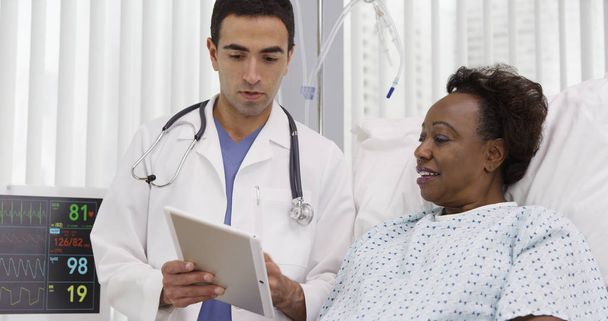 Senior zwarte vrouw liggend in het ziekenhuis kijken naar draagbare tablet pc - Foto, afbeelding