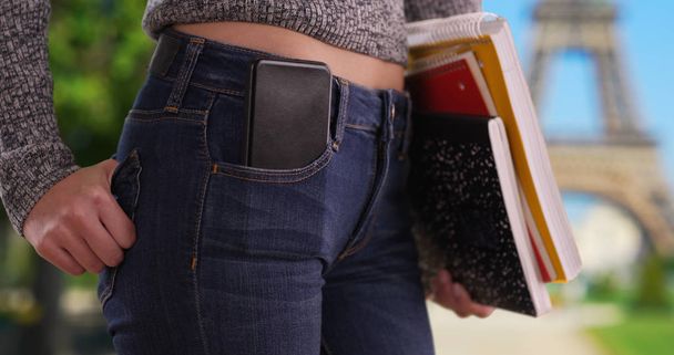 Primer plano de la chica universitaria llevando libros con teléfono en el bolsillo por la Torre Eiffel
 - Foto, Imagen