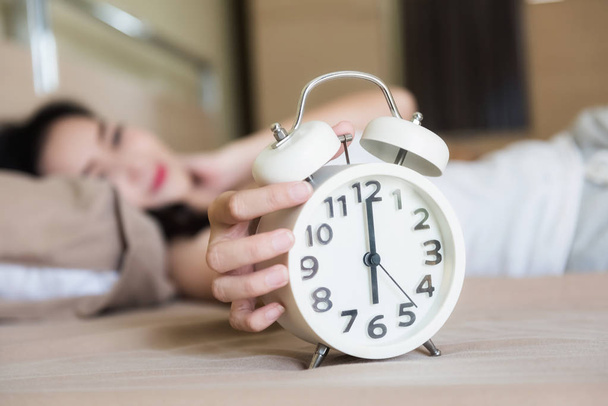 Aziatische mooie vrouw wakker op bed wit wekker uitschakelen om 6 uur in haar slaapkamer. Alarm instellen om op te staan om te gaan werken in een weekdag. - Foto, afbeelding