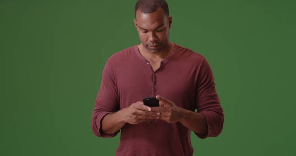 ein schwarzer Mann textet auf seinem Handy auf grünem Bildschirm - Foto, Bild