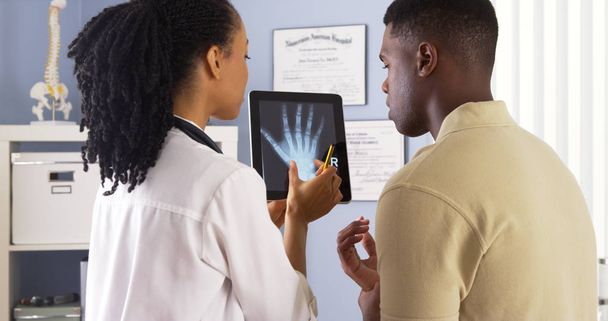 Médico negro compartiendo rayos X de la mano con paciente en el comprimido
 - Foto, Imagen