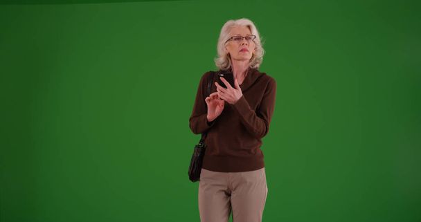 Volwassen witte vrouwelijke gebruiken smartphone om te zoeken van de bestemming op groen scherm - Foto, afbeelding