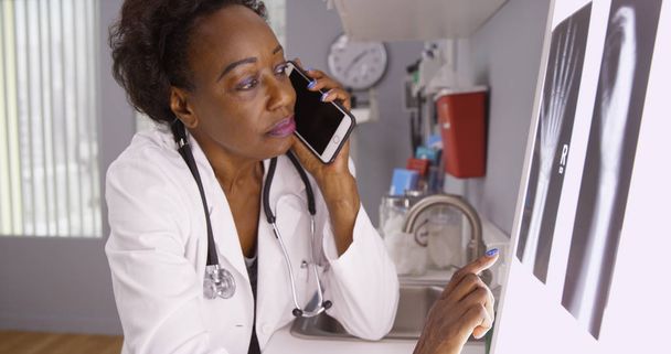 Portrait of African female doctor communicating on phone with colleague on xrays - Photo, Image