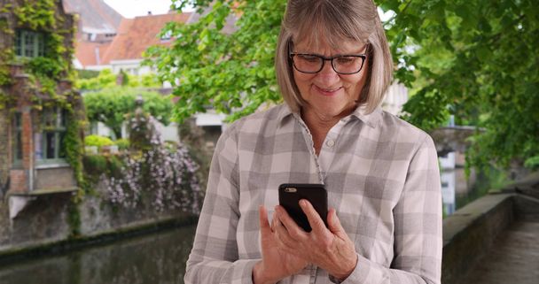Bruges Belçika'iletişim kurmak için taşınabilir teknoloji kullanarak büyüleyici yaşlı kadın - Fotoğraf, Görsel