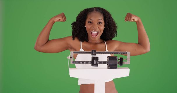 緑色の画面上のスケールにカメラの立っている腕を屈曲健康的な黒人女性 - 写真・画像