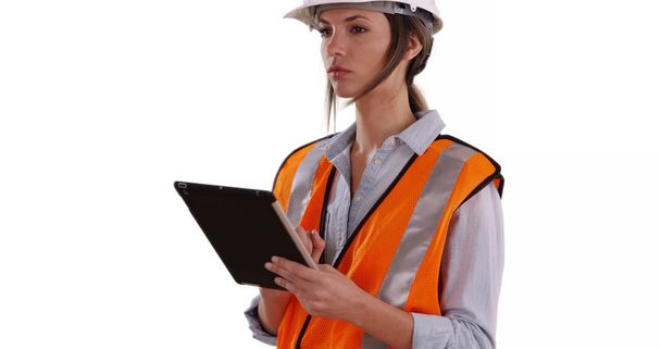 Mulher vestindo colete laranja e chapéu duro trabalhando em tablet em fundo branco
 - Foto, Imagem