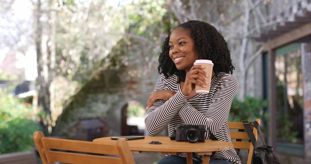 Ελκυστική μαύρη γυναίκα που κάθεται στο τραπέζι σε υπαίθρια ρύθμιση πίνοντας καφέ - Φωτογραφία, εικόνα