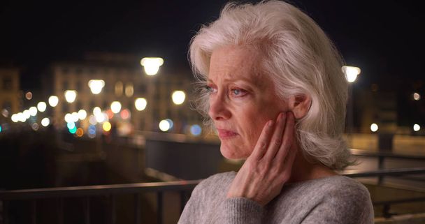 Primer plano de la triste mujer mayor con dolor de cabeza en la ciudad por la noche
 - Foto, imagen