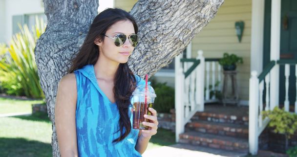 Mixed race woman standing by tree drinking iced tea - Photo, Image