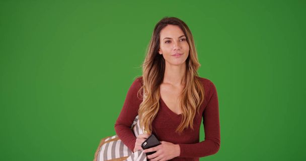 Young woman with a purse and a mobile phone smiling on green screen - Foto, Bild