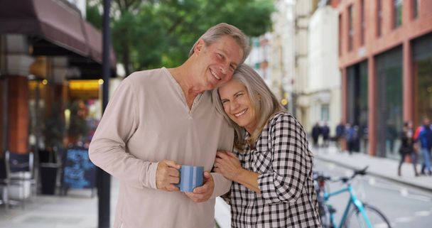 Older loving Caucasian couple snuggles on London sidewalk - Photo, Image