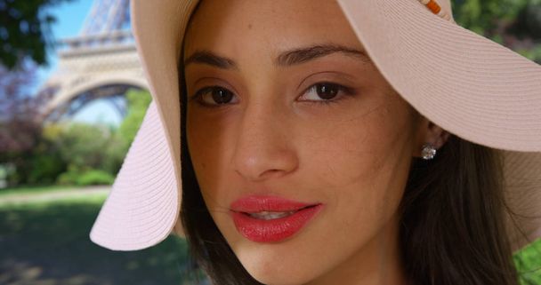 Cute Hispanic female in stylish hat smiles at camera near Eiffel Tower - Photo, Image