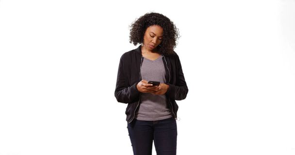 Ξέγνοιαστες Αφροαμερικανός νεαρή κοπέλα τον έλεγχο του τηλεφώνου σε λευκό φόντο - Φωτογραφία, εικόνα