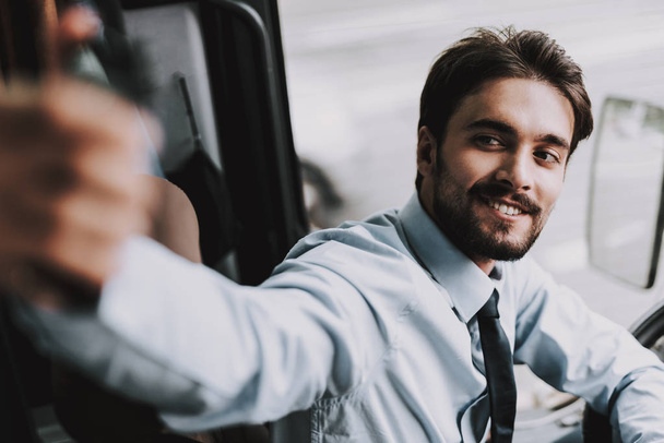 Smiling Man Driving Tour Bus. Professional Driver. Young Happy Man wearing White Shirt and Black Tie Sitting on Driver Seat. Attractive Confident Man at Work. Traveling and Tourism Concept - Foto, Imagem