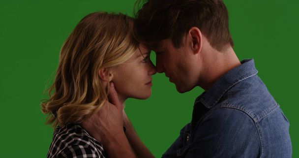 Young white couple looking into each other's eyes ready to kiss on green screen - Photo, Image