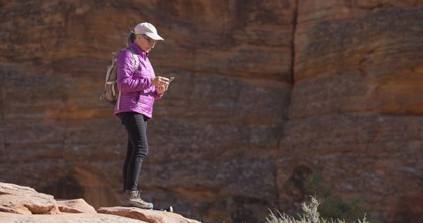 Healthy elderly woman in sandstone canyon with mobile device sending photos  - Foto, Imagem