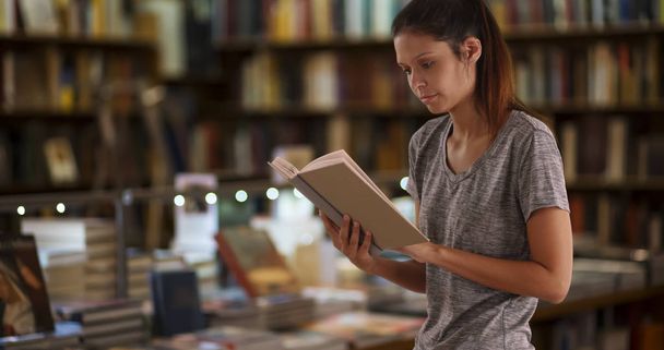Mooie jonge vrouw lezing in bibliotheek door bookstacks - Foto, afbeelding
