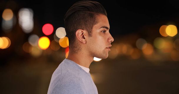 Oldalnézet fiatal Y-generációs férfi alákínálással áll odakint éjszaka fények és utcák a háttérben - Fotó, kép